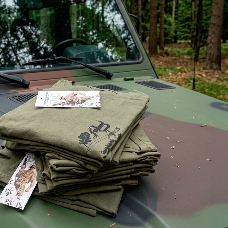 Ein Stabel T-Shirts der auf einer Bundeswehr Mercedes G-Klasse in Tarnfarben liegt